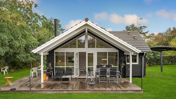 Uma casa moderna com fachada envidraçada, deck de madeira e mobiliário para área externa.