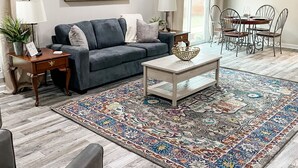 A living room with a grey sofa, a coffee table, a patterned rug, a dining area with metal chairs, and a ceiling fan. - Two-Seventeen, a cozy Wetumpka home (Wetumpka)