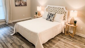 A bedroom with a large bed, two bedside tables with lamps, a painting on the wall, and wooden flooring. - Two-Seventeen, a cozy Wetumpka home (Wetumpka)