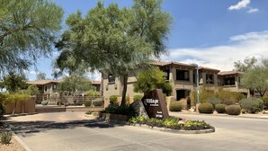 En lukket indgang med et skilt der siger "Village at Grayhawk" og en bygning med tegltag og stukkede vægge.