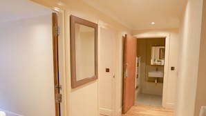 A hallway with wooden flooring, a mirror on the wall, and a bathroom visible through an open door.