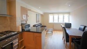 A modern kitchen with a gas stove, microwave, and wooden cabinets. There is a dining area with a table and chairs, and a window providing natural light.