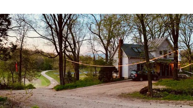 A rural road leading to a house surrounded by trees.