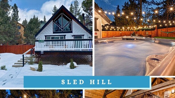 A cabin with a deck, a snow-covered yard, a lit outdoor area, and a cozy interior with a fireplace and leather furniture.