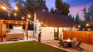A backyard with a hot tub, wooden deck, and string lights.