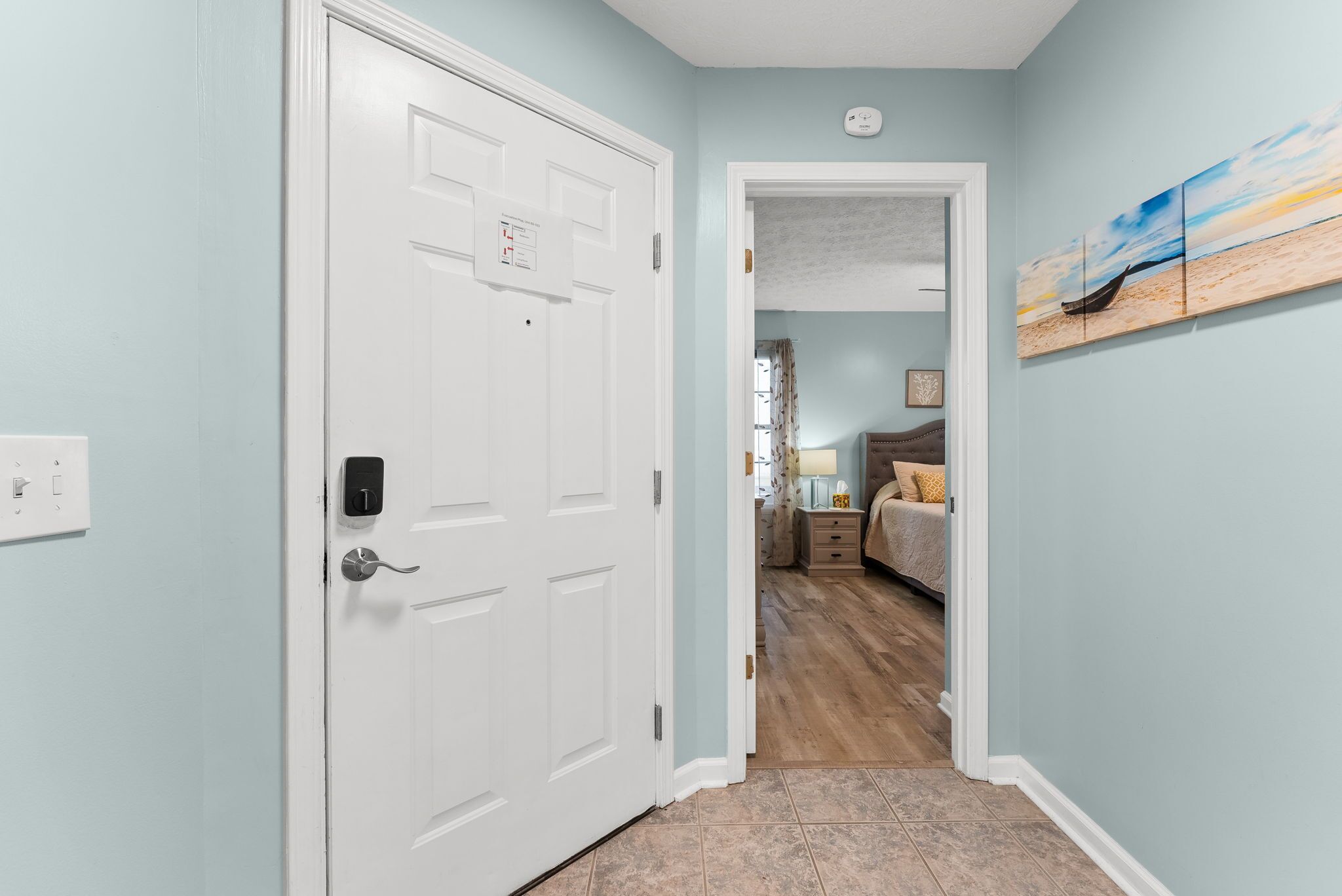 A hallway leading to a bedroom with a bed, a nightstand, and a wall-mounted artwork.