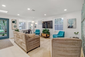 A living room with a sofa, two armchairs, a coffee table, a TV, and a dining area with a table and chairs.
