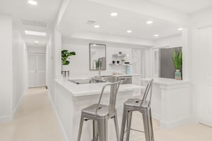 A modern kitchen with white countertops, stainless steel appliances, and two bar stools.