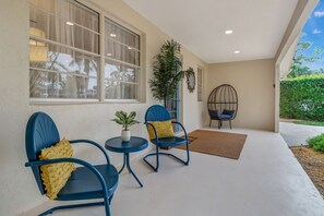 Un patio cubierto con dos sillas azules, una mesita y una planta en maceta.