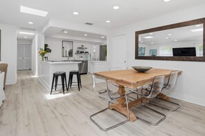 A modern kitchen with white cabinetry, a central island, and a dining area with a wooden table and clear chairs.
