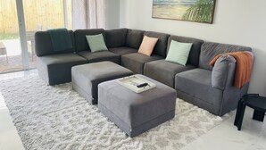 Ein modernes Wohnzimmer mit einem grauen Ecksofa, einem weißen Shaggy-Teppich und einem Gemälde mit einer Strandansicht.