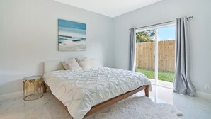Ein Schlafzimmer mit einem Bett, einem Nachttisch, einem Gemälde und Blick ins Freie.