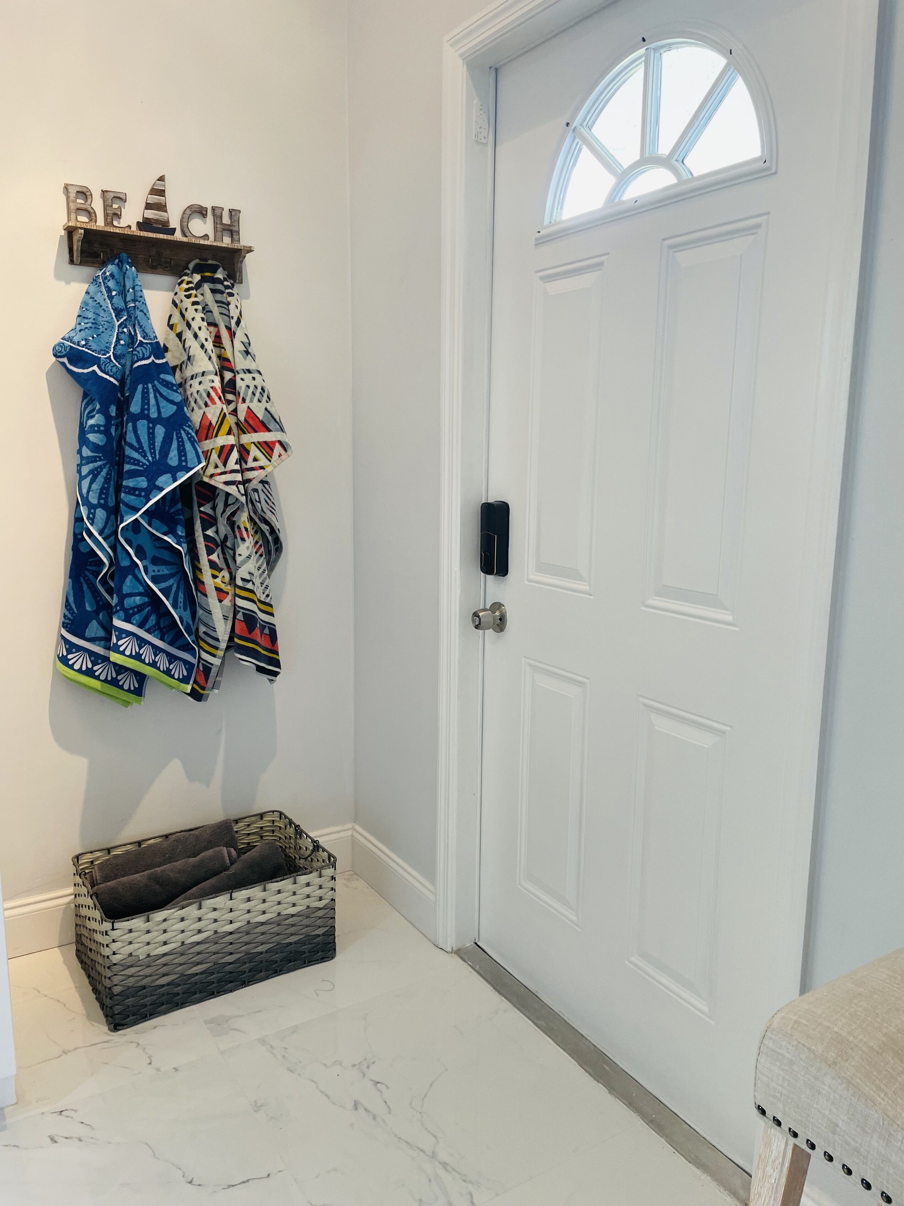 A white door with a small window, a wall-mounted coat rack with patterned jackets, and a wicker basket on the floor.