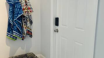 A white door with a small window, a wall-mounted coat rack with patterned jackets, and a wicker basket on the floor.