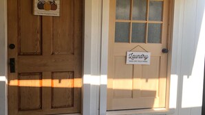 A wooden door with a welcome sign and a laundry sign, and two wooden benches in front. - Studio B. Katie and Steve Riley Apartment (Breaux Bridge)
