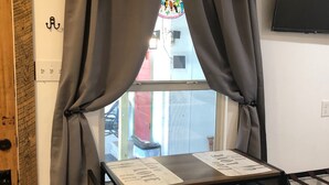 A room with a window, a table with two chairs, a TV mounted on the wall, and a wooden door. - Studio B. Katie and Steve Riley Apartment (Breaux Bridge)