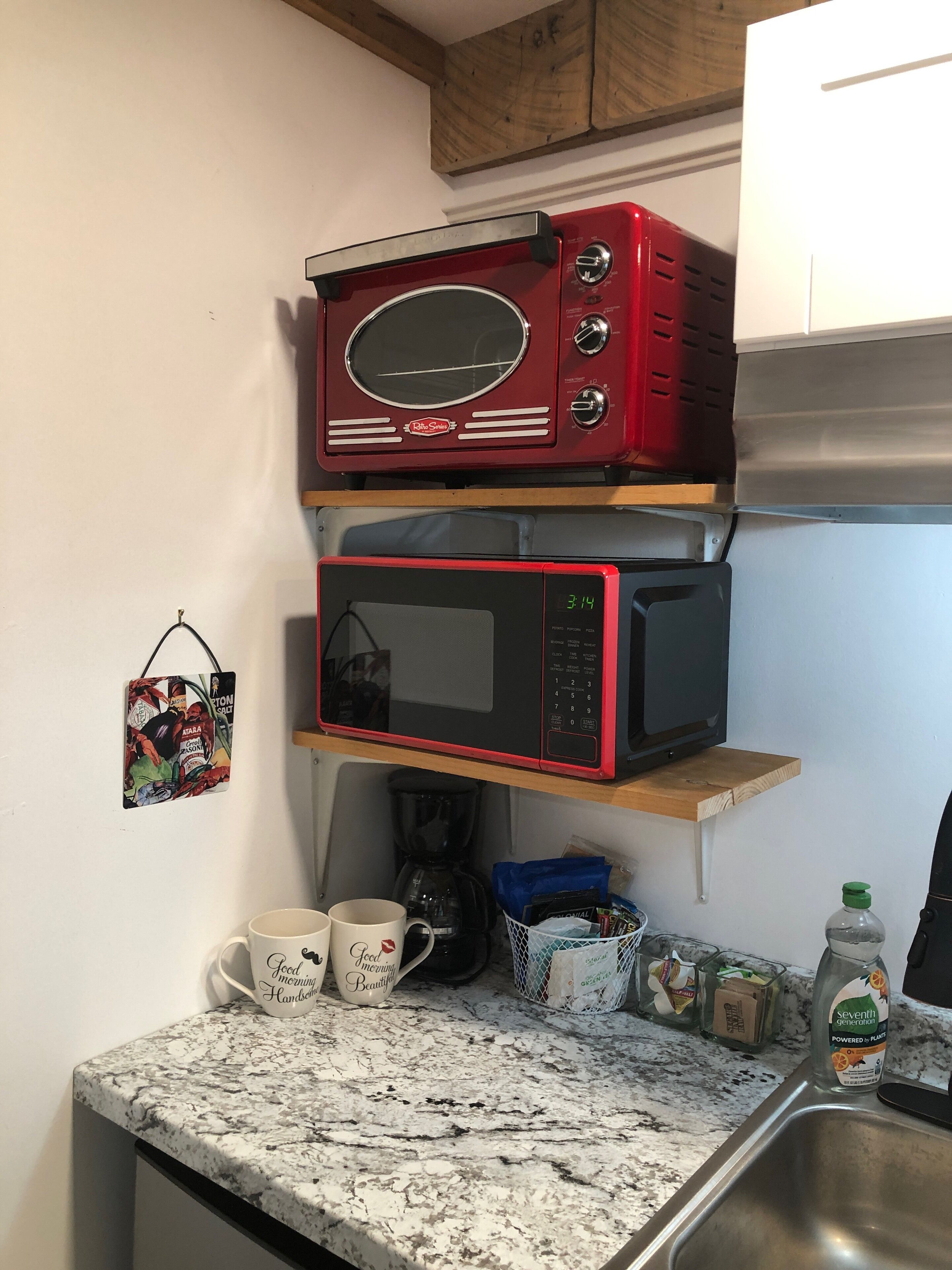 A kitchen with a microwave on a shelf, a coffee maker, and a bottle of Seventh Generation water.