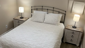 A bedroom with a bed, two bedside tables, a nightstand, a window with curtains, and a ceiling light fixture.
