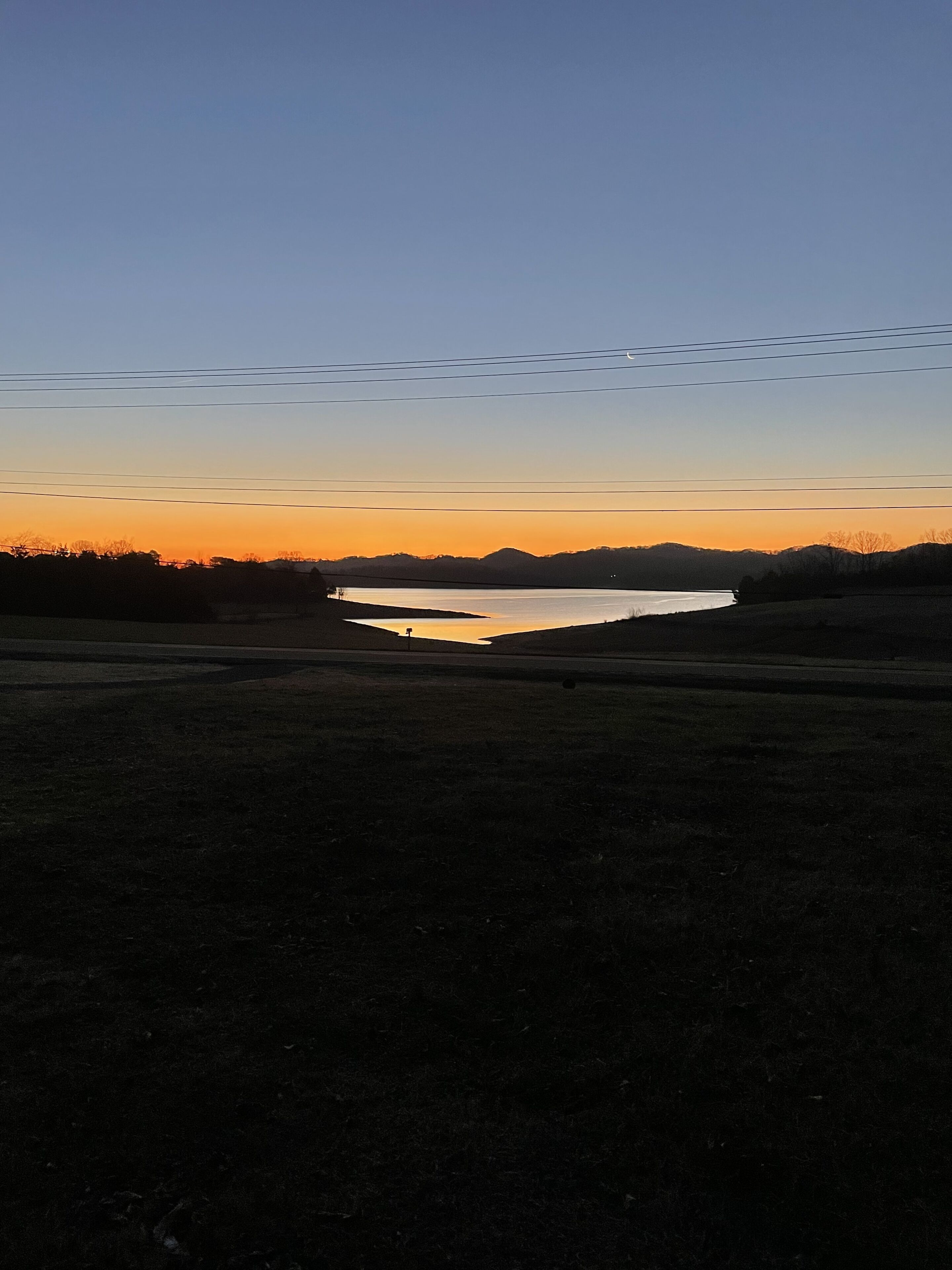 A sunset over a lake with a clear sky and distant hills.