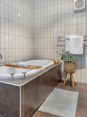 Une salle de bain moderne avec une baignoire sur pieds, un plateau en bois, une plante en pot et un tapis à motifs.