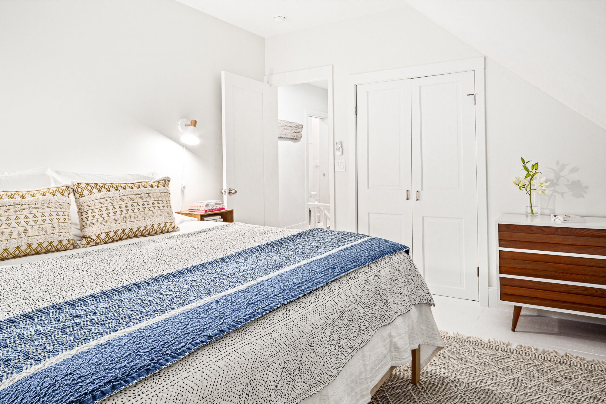 A bedroom with a bed, bedside table, lamp, wardrobe, and a dresser.
