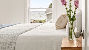 Une chambre à coucher avec un lit, une table de chevet avec une lampe, une fenêtre donnant sur le port et un appareil de climatisation.