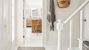 Un couloir avec un escalier, un panier en osier et une serviette rayée accrochée au mur.