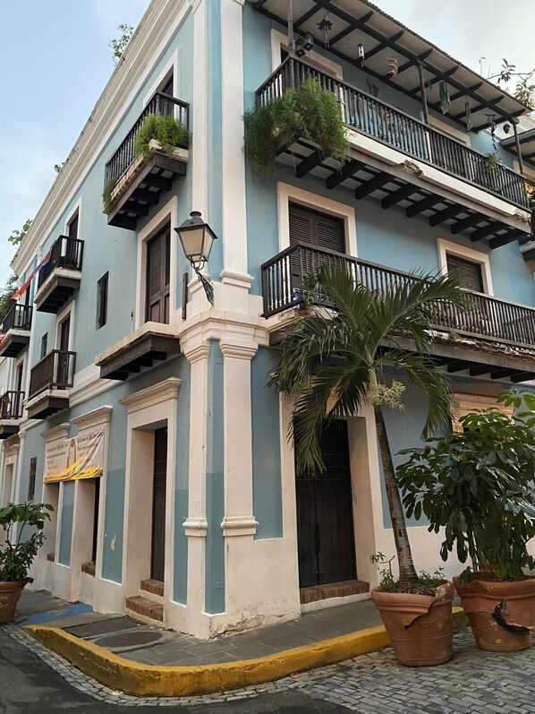 Un edificio de varios pisos con balcones, plantas en macetas y vista a la calle.