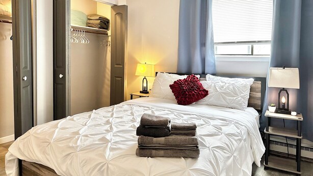 Ein Hotelzimmer mit Bett, Nachttisch, Lampe, einem Fenster mit Vorhängen und einem Kleiderschrank.