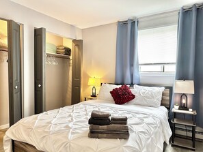 A hotel room with a bed, a nightstand, a lamp, a window with curtains, and a wardrobe. - Comfy beds/Fast wifi/Getaway/Free Parking/Raging Waves Water park (Aurora)