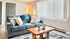 Ein Wohnzimmer mit grauem Sofa, einem Holztisch und einem gemusterten Teppich.