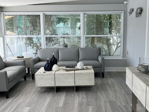Relax in this stylish living room with a grey sofa, coffee table, and views of lush greenery outside.