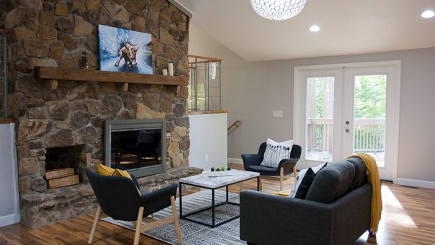 A living room with a stone fireplace, a sofa, a coffee table, and a view of the outdoors.