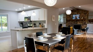 A modern kitchen with white cabinets, a stone accent wall, and a dining area with a wooden table and black chairs.