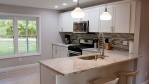 A modern kitchen with white cabinets, a granite countertop, and a large window.