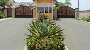 A residential property with a gated entrance, a small house with a sloped roof, and a well-maintained garden with various plants and flowers. - Stunning townhouse in gated community -10 minutes from three beaches. (Mount Pleasant)