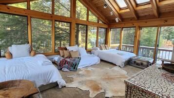 A cabin with three beds, a wooden ceiling, large windows, and a stone fireplace.