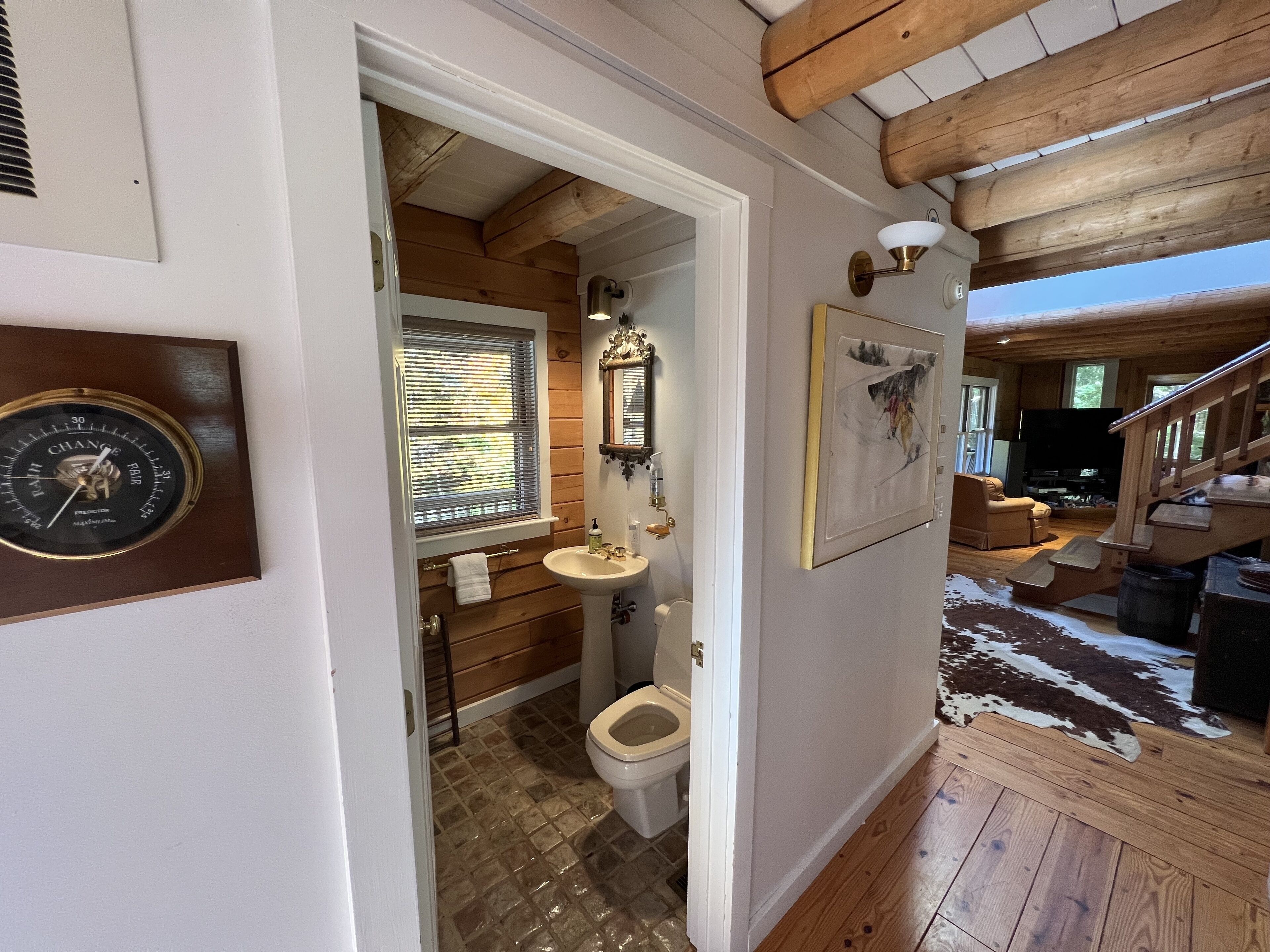 A wooden interior with a bathroom, a mounted clock, and a mounted picture.
