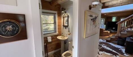 A wooden interior with a bathroom, a mounted clock, and a mounted picture.