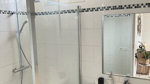 A modern bathroom with a glass shower enclosure, white tiled walls, a black patterned vanity, and a large mirror.