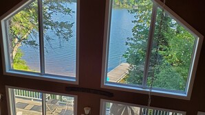 A room with large windows overlooking a lake, a hanging chair, and a small table.