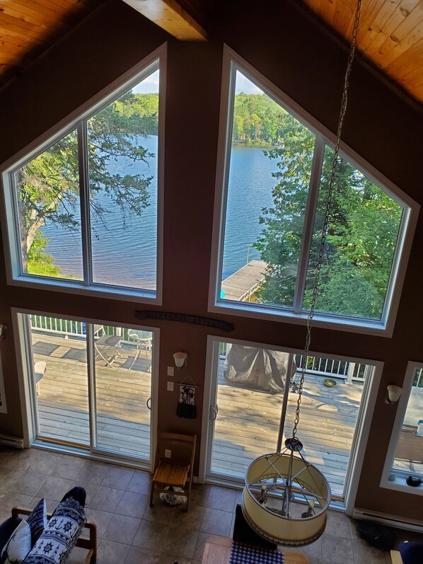 A room with large windows overlooking a lake, a hanging chair, and a small table.