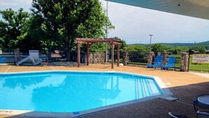 Piscina con pergola, area recintata con lettini e vista su colline sullo sfondo.