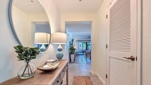 A hallway with a wooden console table, two lamps, a mirror, a potted plant, a rug, and a door with a louvered panel. - Luxury Residence 3BR near 5th Ave & Beach (Naples)