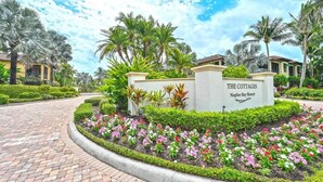 A landscaped entrance with a sign for 'The Cottages Naples Bay Resort,' surrounded by palm trees and flower beds. - Luxury Residence 3BR near 5th Ave & Beach (Naples)