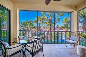 A balcony with a glass table and chairs, a wicker chair, and a view of palm trees and a pool. - Luxury Residence 3BR near 5th Ave & Beach (Naples)