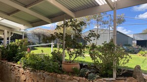 Un patio couvert agrémenté d’un mur en pierre, de plantes en pot et offrant une vue sur une pelouse et des bâtiments en arrière-plan.