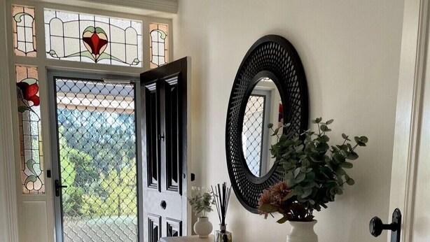Un couloir avec une porte blanche, une console en bois, un miroir et une plante en pot.