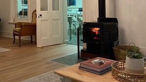 Un salon avec une table basse en bois, un canapé, un lustre, une cheminée et une vue sur une autre pièce, accessible par une porte.