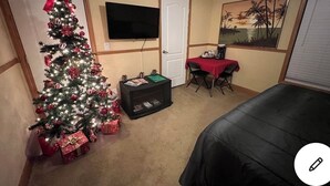 A hotel room with a Christmas tree, a flat-screen TV, a painting, and a dining table with chairs.